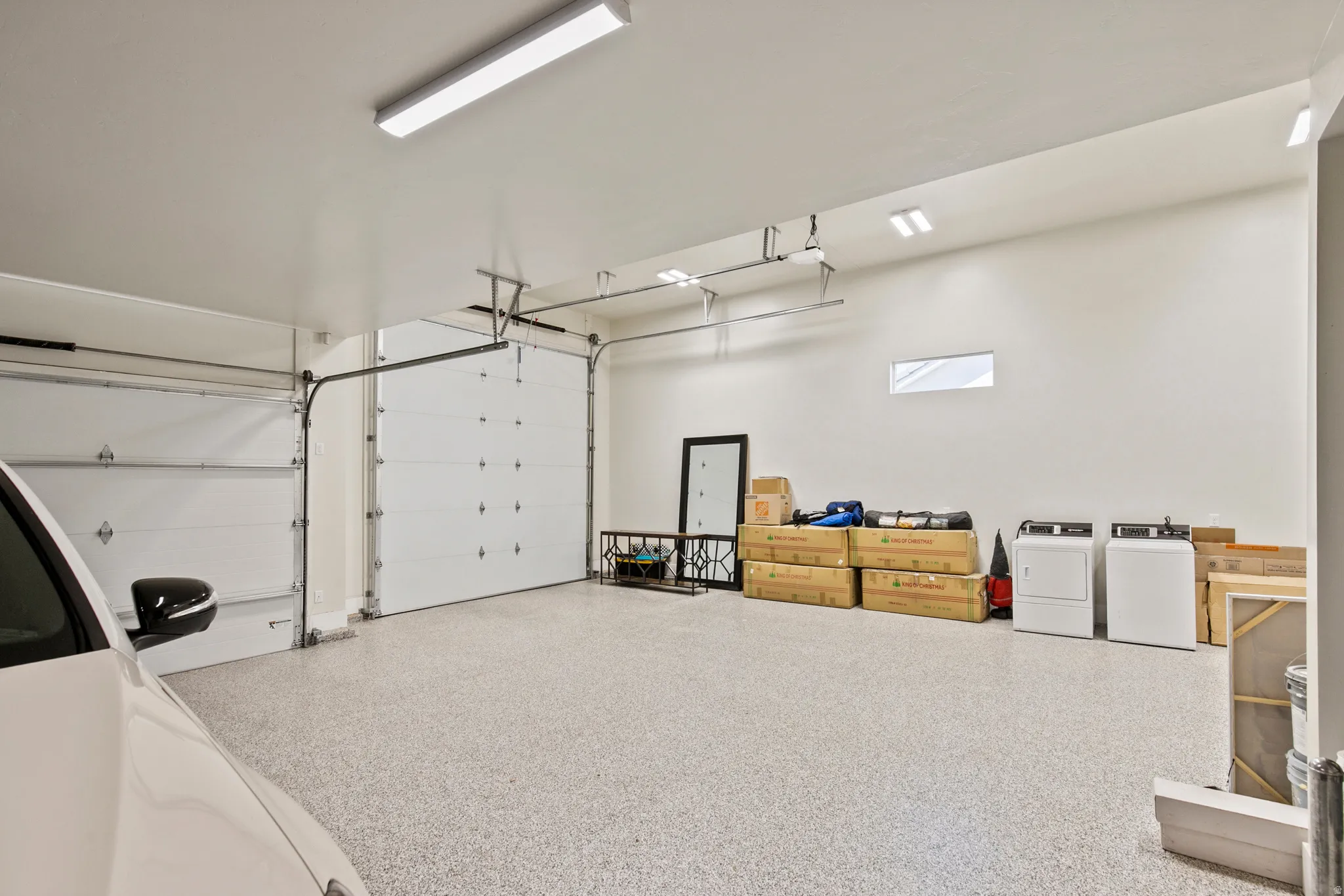 Spacious garage featuring two overhead doors, a light-colored speckled floor coating, high ceilings, and recessed lighting