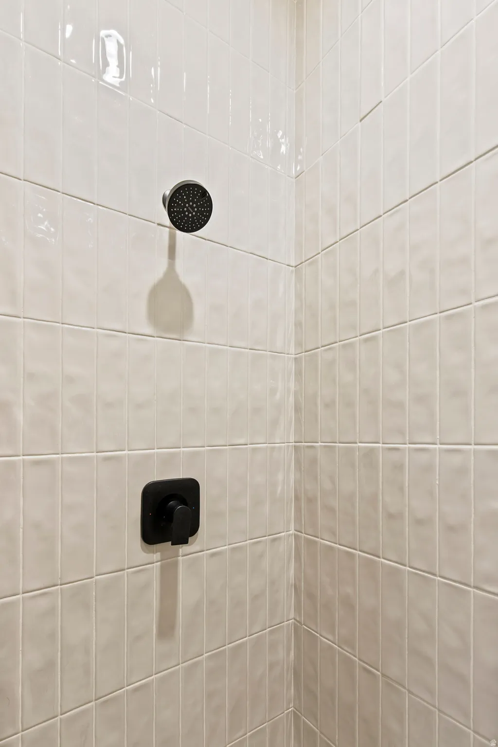 Shower enclosure featuring white vertical subway tile, a matte black shower head, and a coordinating matte black control handle