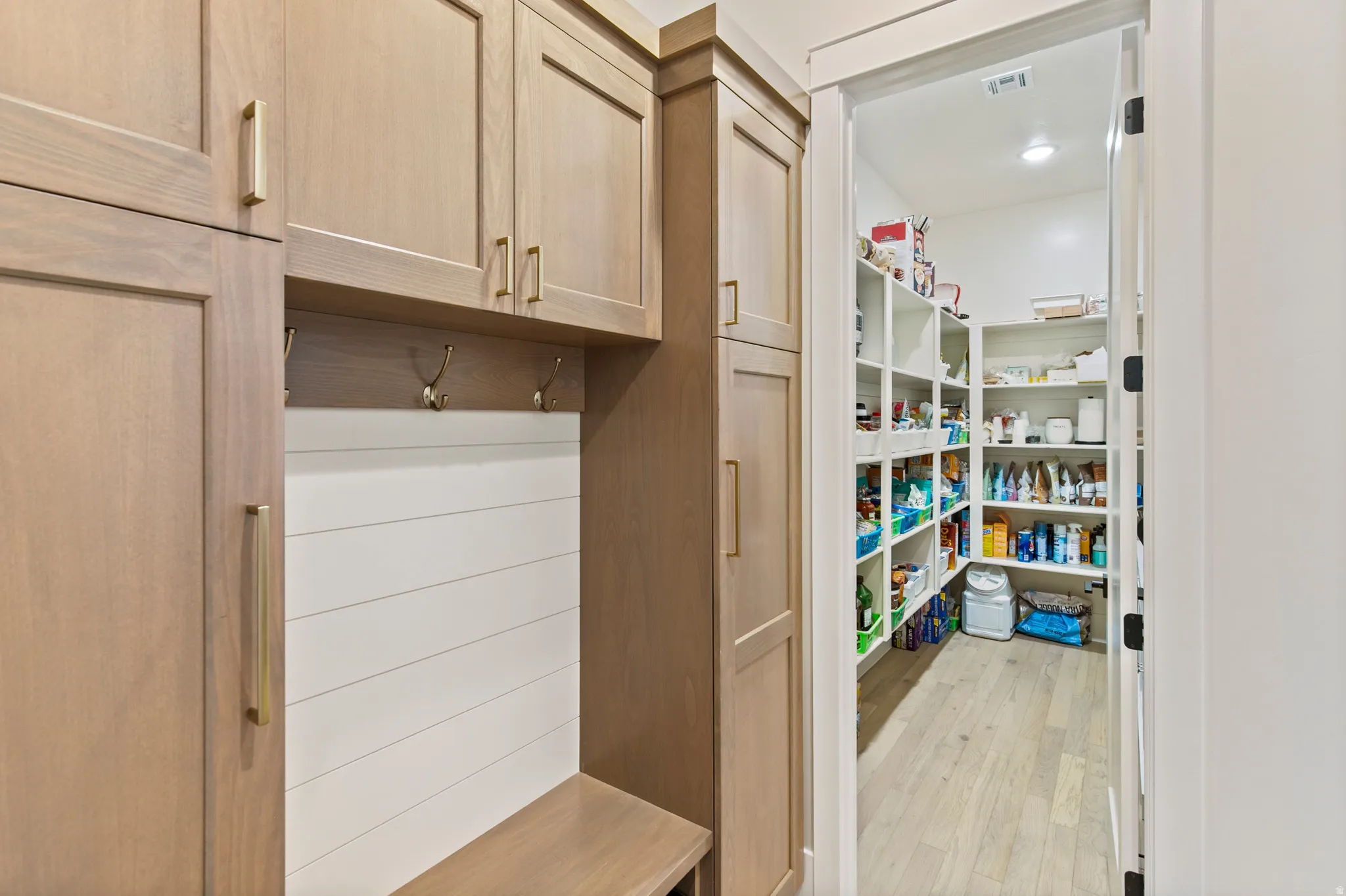 Built-in mudroom cabinetry with a bench seat and brass hooks