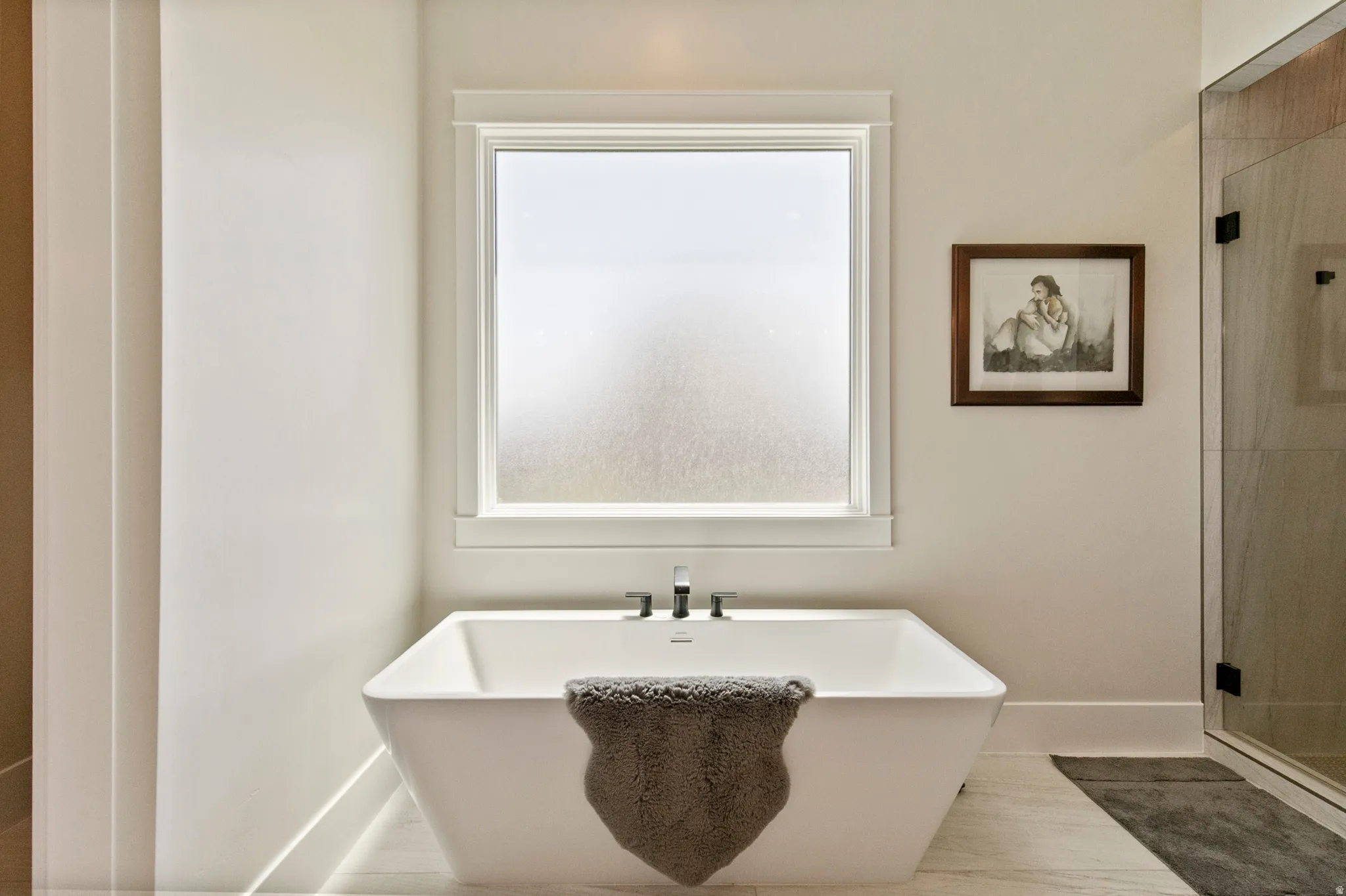 Freestanding soaking tub with a wall-mounted faucet, frosted privacy window, and large format floor tile