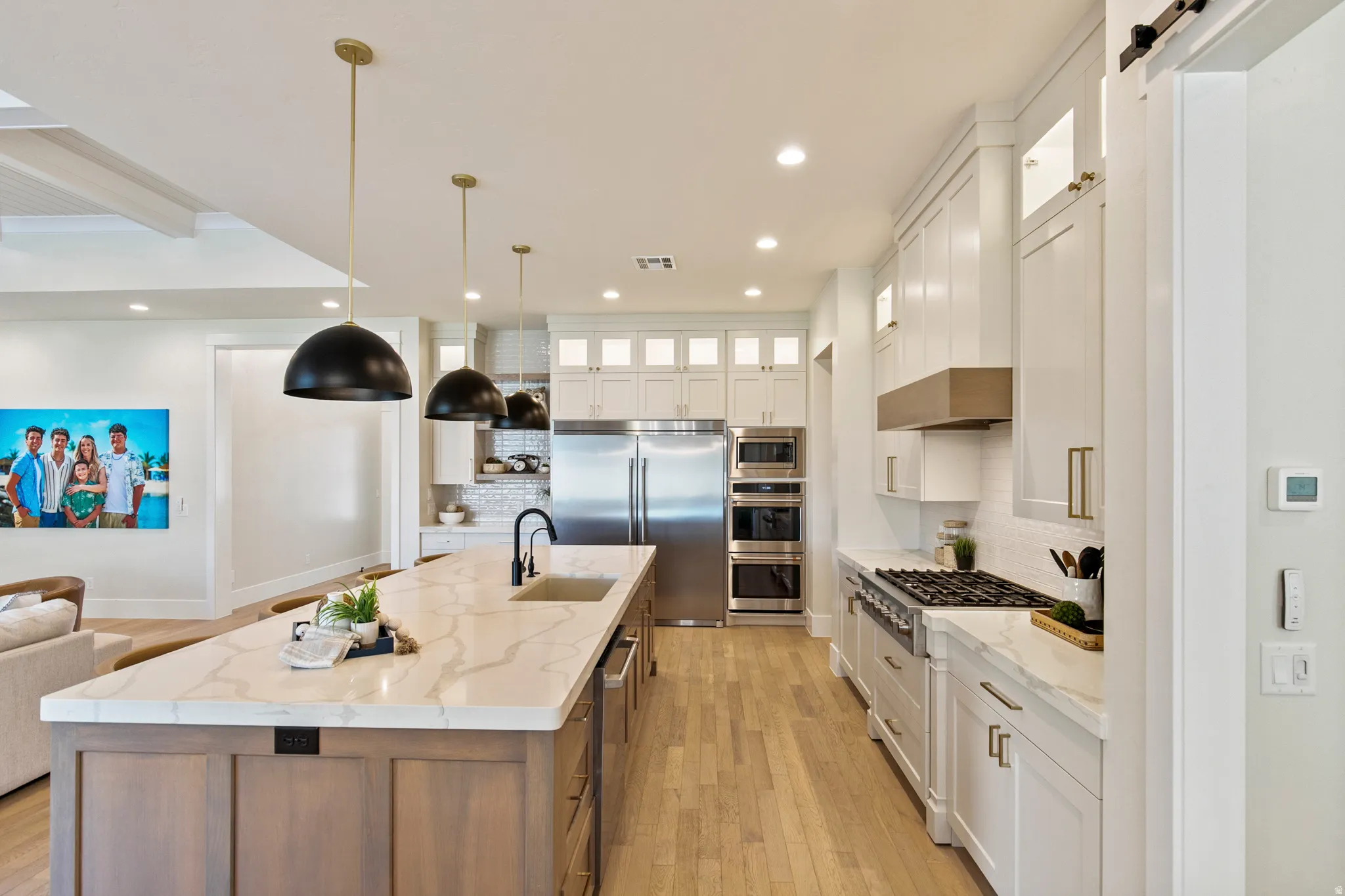 Gourmet kitchen featuring a substantial island with integrated sink, dual pendant lighting, stainless steel appliances, and wood-finish flooring