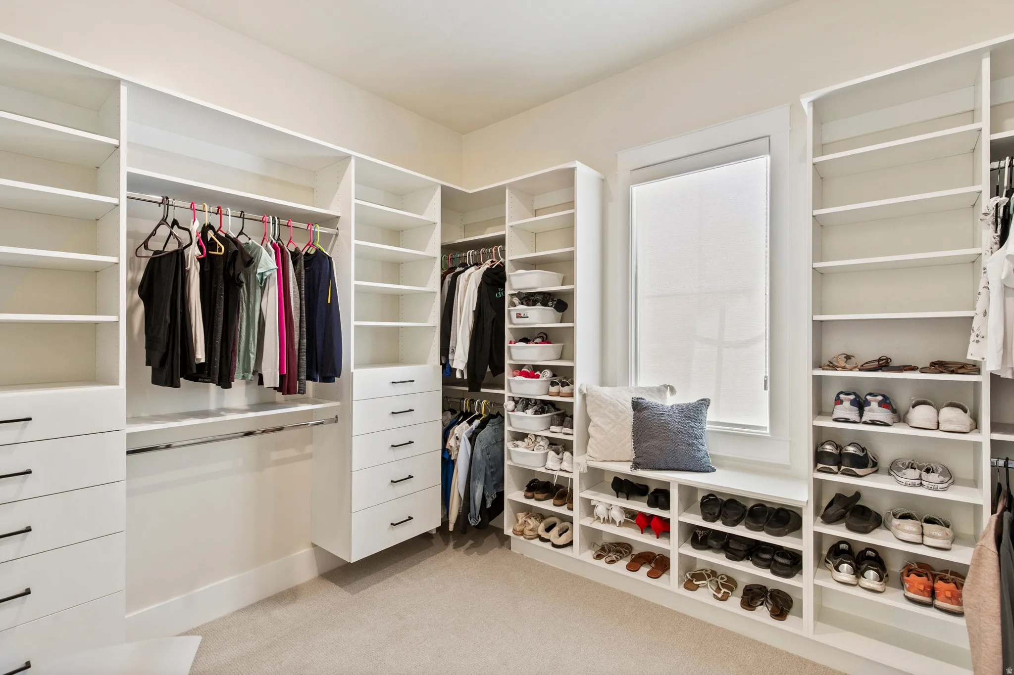 Custom closet system featuring extensive shelving, built-in drawer units, multiple hanging rods, a window-integrated seating bench, and dedicated shoe storage