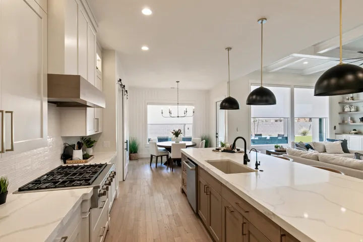 Expansive kitchen featuring a large island with sink, gas range with hood, white subway tile backsplash, and light wood-finish flooring