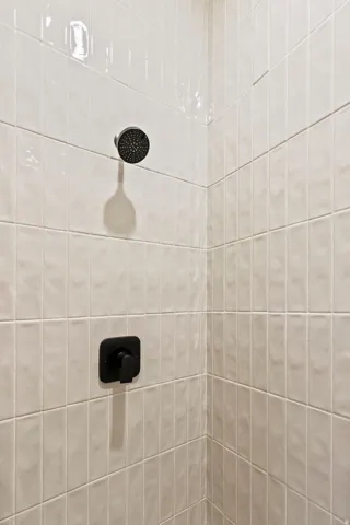 Shower enclosure featuring white vertical subway tile, a matte black shower head, and a coordinating matte black control handle