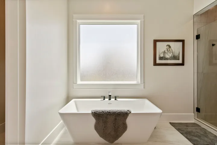 Freestanding soaking tub with a wall-mounted faucet, frosted privacy window, and large format floor tile