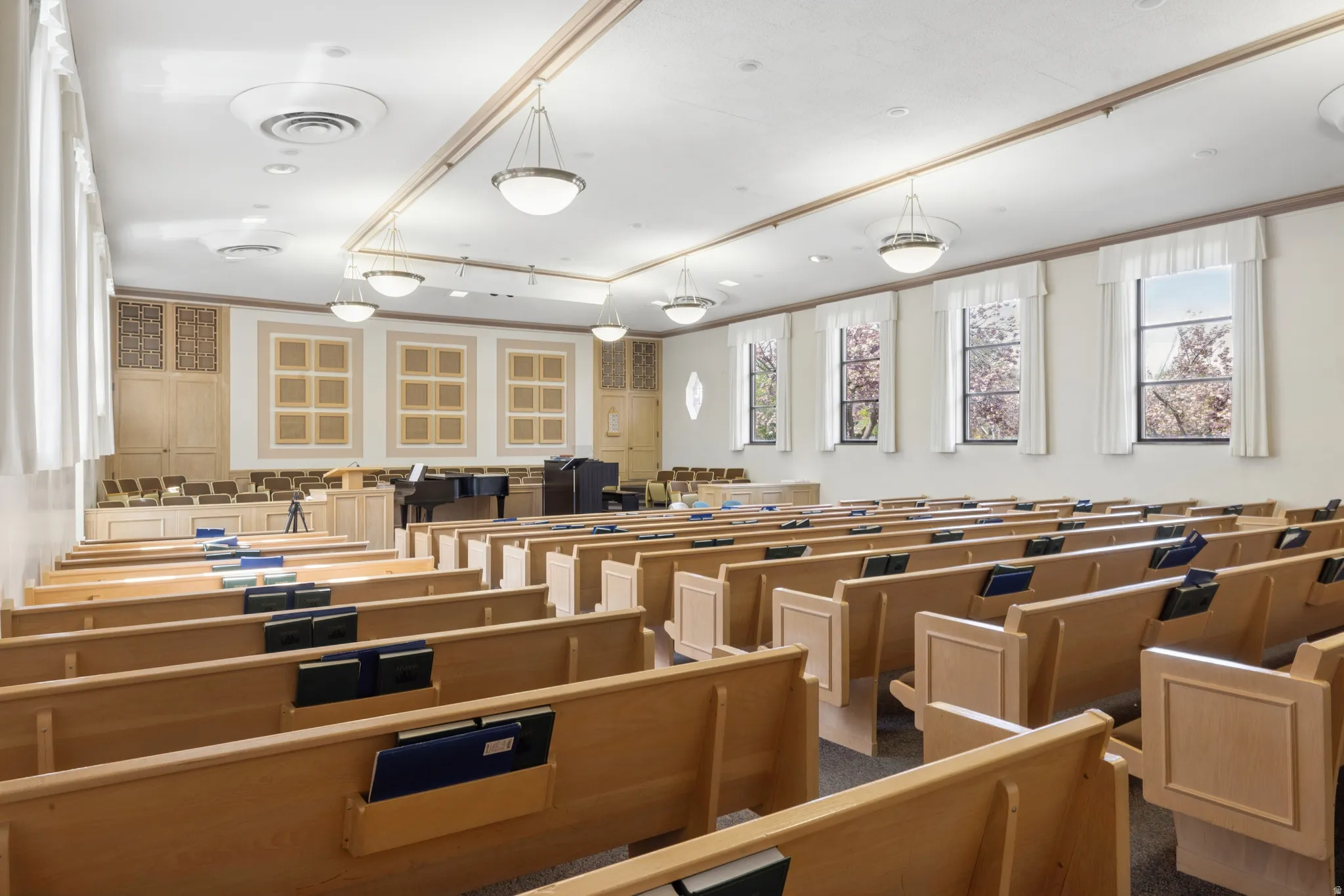 Large open hall featuring rows of wooden pews and overhead chandelier lighting fixtures