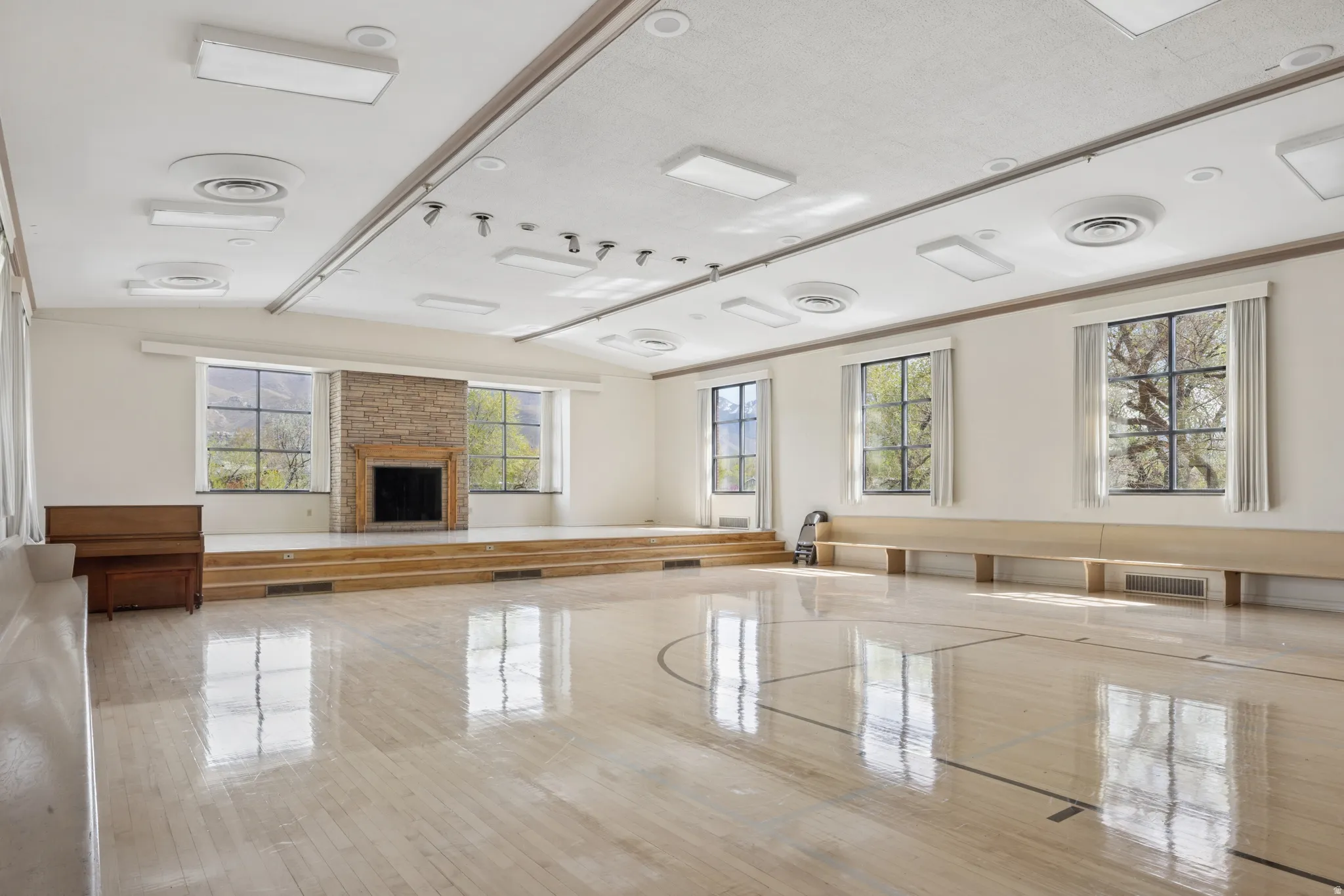 Spacious room featuring wood-finish flooring, a raised platform with integrated steps, and a stone-clad fireplace
