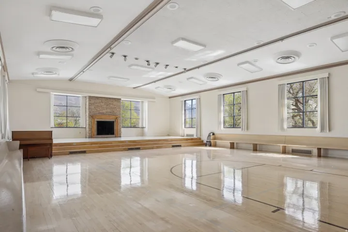 Spacious room featuring wood-finish flooring, a raised platform with integrated steps, and a stone-clad fireplace
