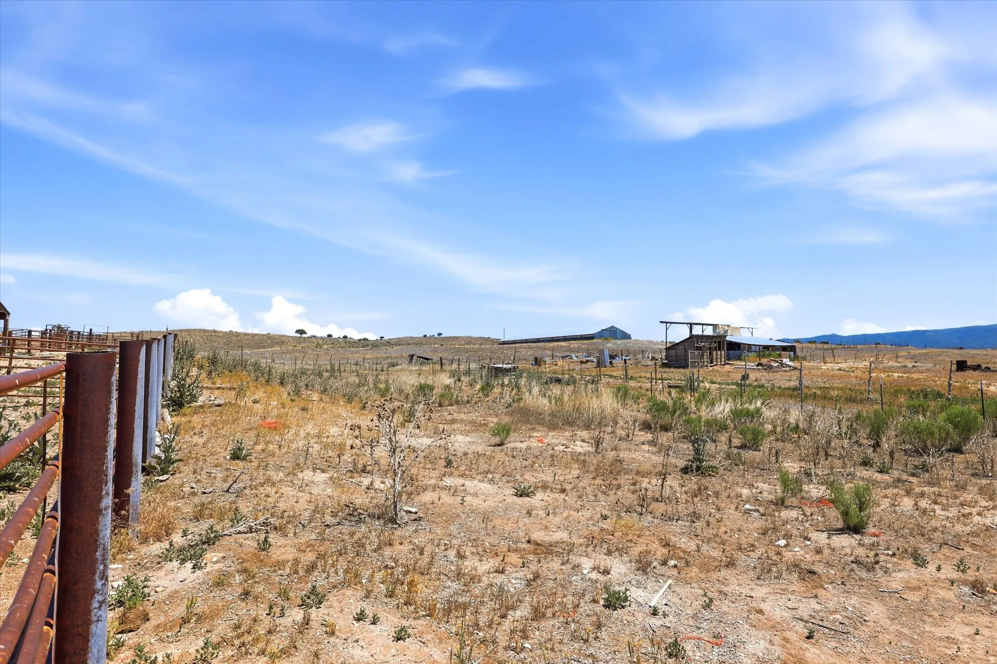 Expansive land parcel featuring existing fencing, a distant outbuilding, and a clear sky above.  ***Seller and their agents DO NOT assume liability for anyone that goes near or inside the structures.  Please observe from a cautious distance and consult wi
