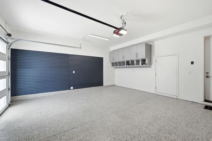 Spacious garage featuring a durable epoxy floor, slatwall storage system, overhead cabinetry, and an automatic garage door opener