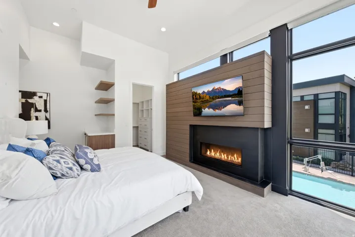 Carpeted room featuring a modern linear fireplace with wood-finish paneling, floor-to-ceiling windows, and a walk-in closet with built-in shelving
