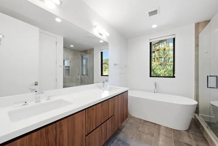 Modern bathroom featuring a wood-finish double vanity with integrated sinks and white countertops, a freestanding soaking tub, a glass-enclosed shower, and tile flooring
