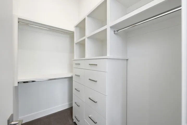 Walk-in closet featuring white built-in cabinetry, shelving, multiple hanging rods, and drawers with brushed nickel pulls