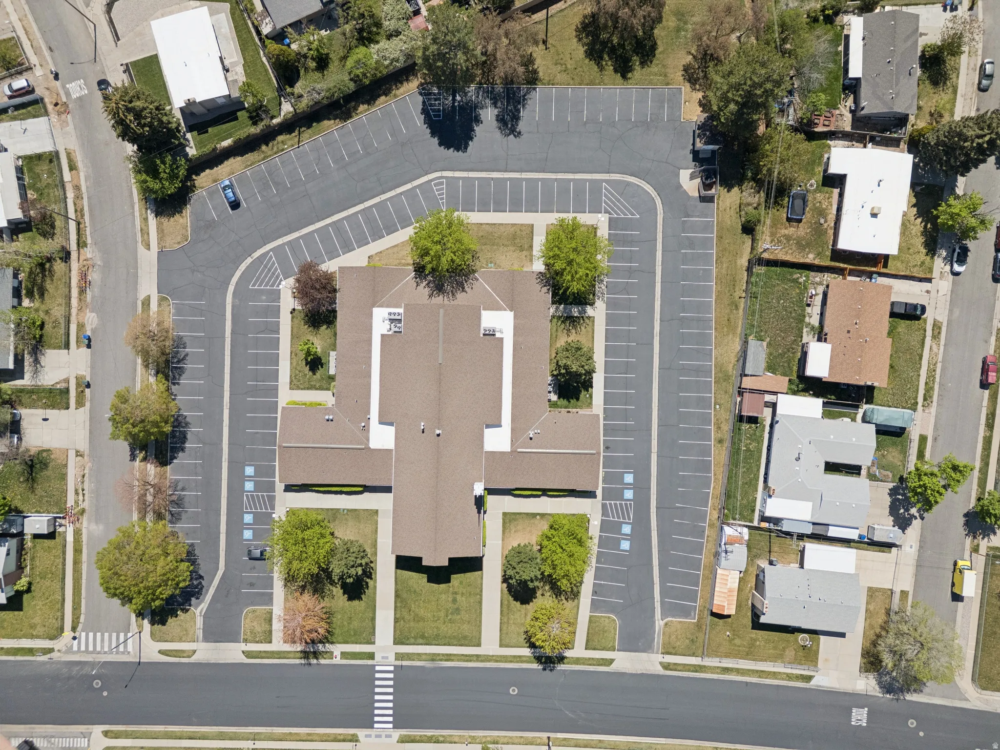 Expansive property featuring a large building with a multi-gabled roof, extensive asphalt parking with marked spaces, surrounding green lawns, and mature trees