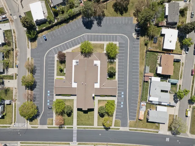 Expansive property featuring a large building with a multi-gabled roof, extensive asphalt parking with marked spaces, surrounding green lawns, and mature trees