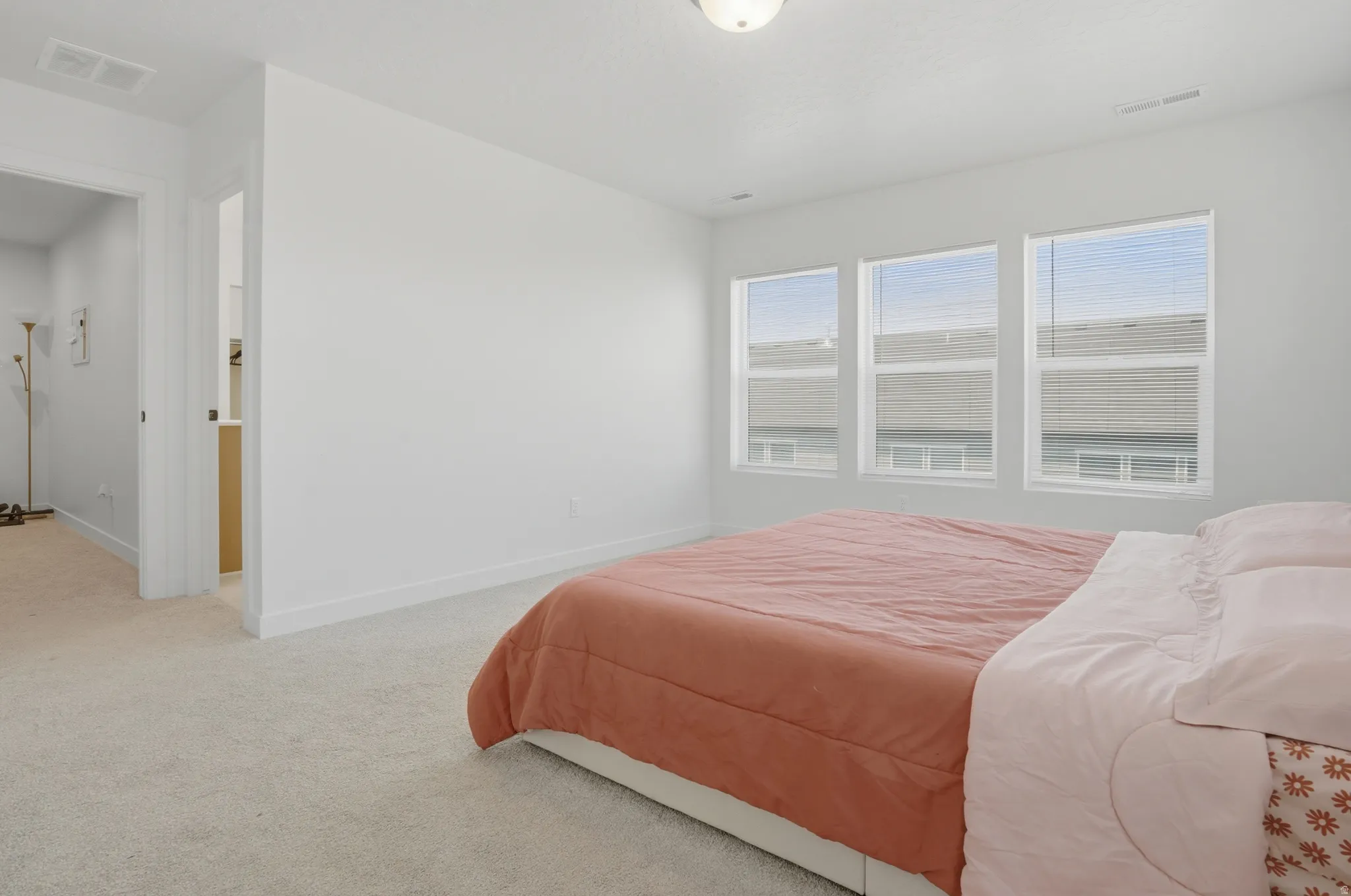 Bright interior room featuring three windows, light-colored carpeting, white walls, and white baseboards