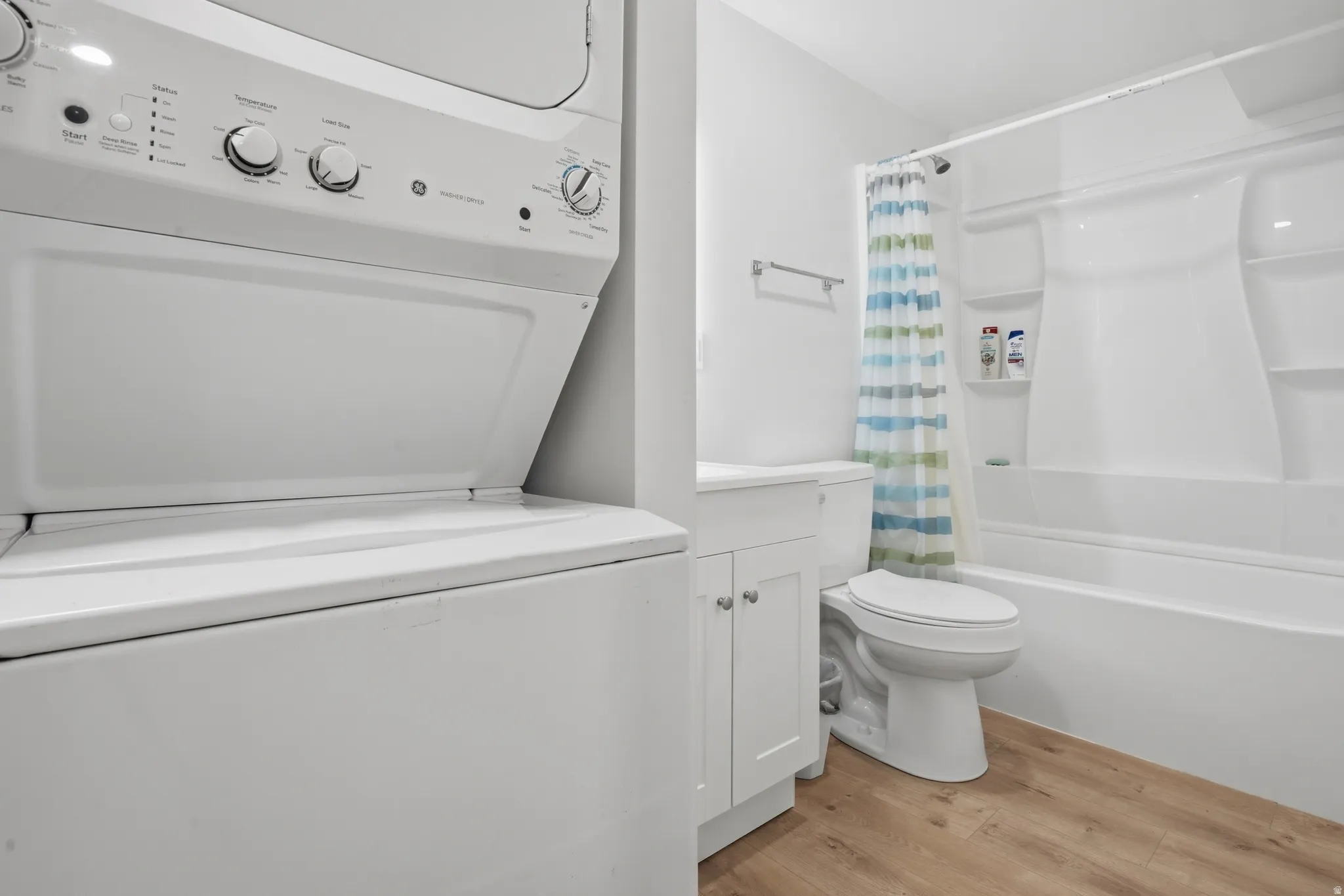 Bathroom featuring wood-finish flooring, a white vanity with cabinet storage, a toilet, and a white tub and shower combination with an integrated shelf
