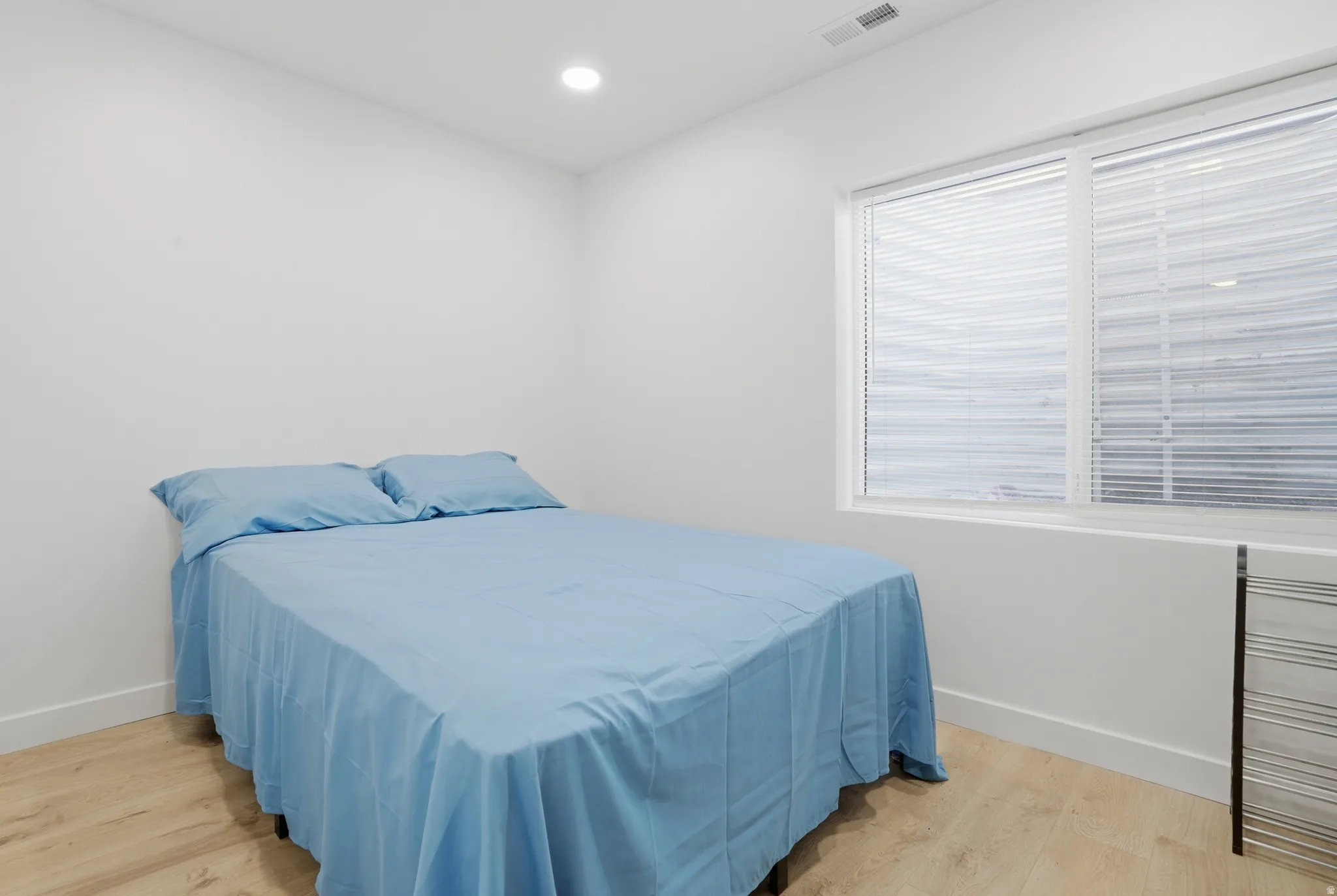 Bright room featuring a large window with horizontal blinds, wood-finish flooring, white baseboards, and recessed lighting