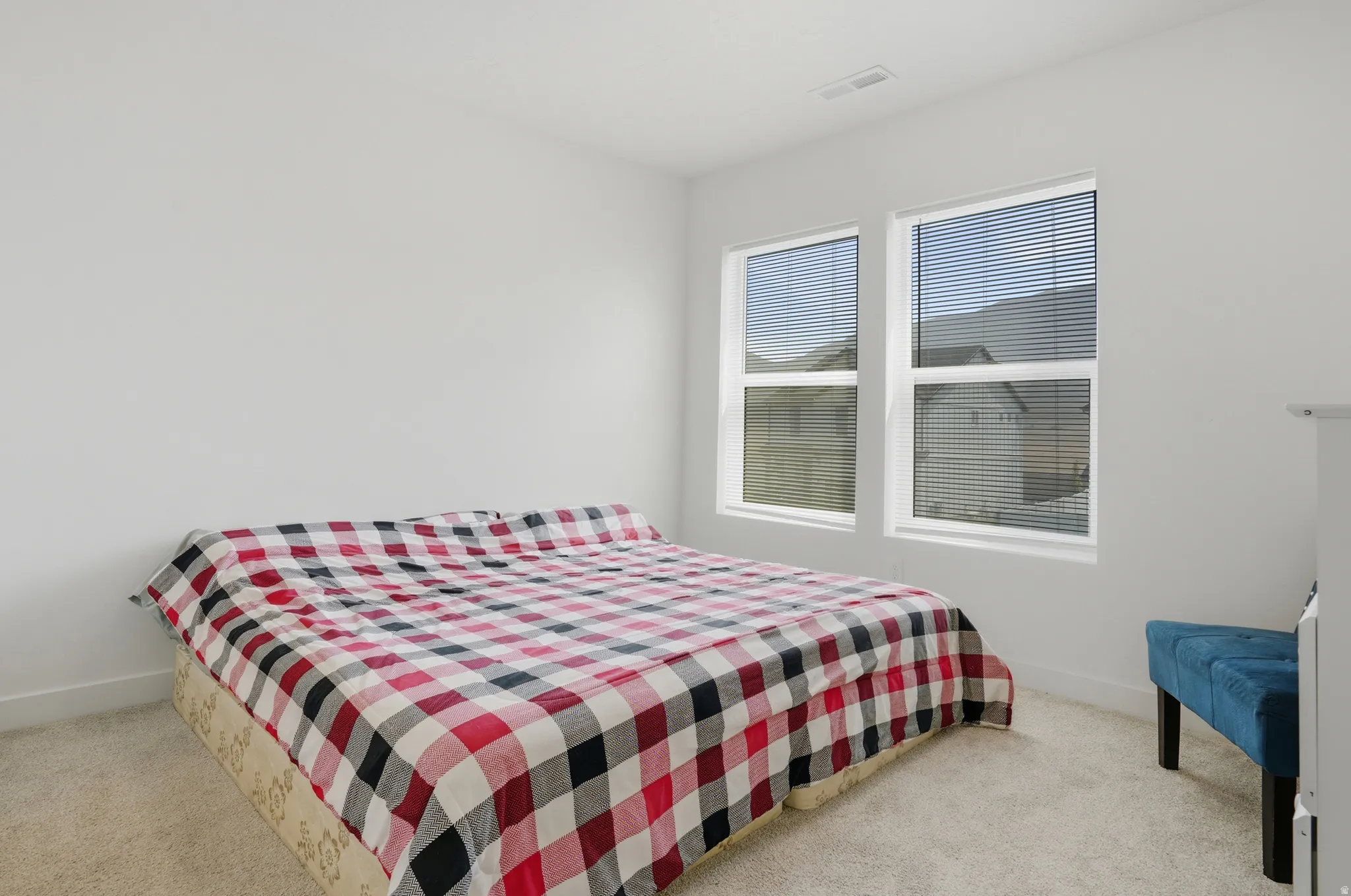 Bright interior space featuring two windows with horizontal blinds, neutral wall paint, and light-toned carpeting