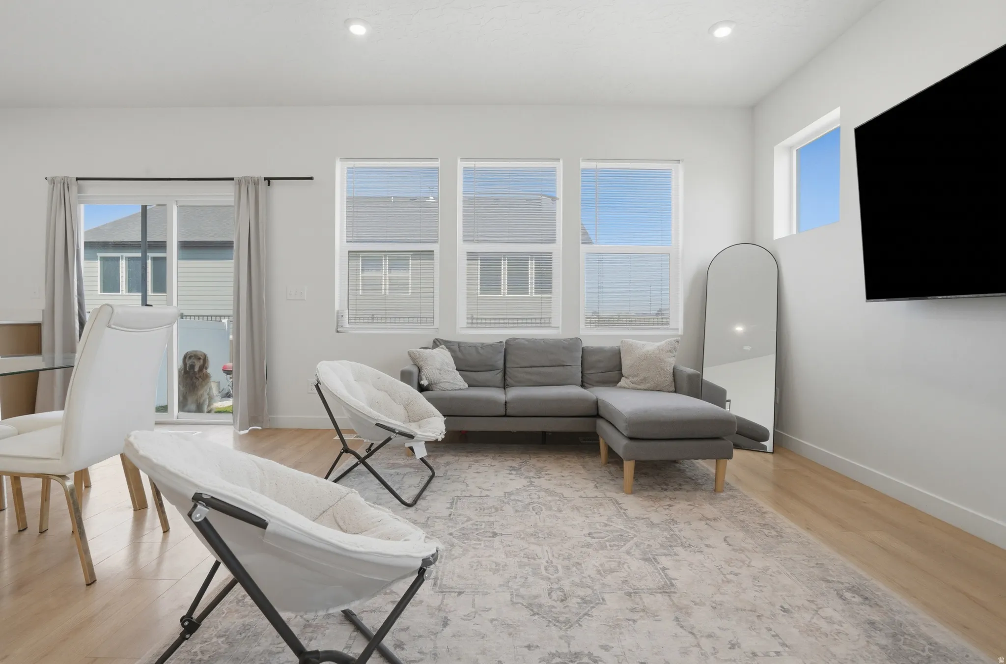 Living area featuring wood-finish flooring, recessed lighting, white walls, multiple windows with blinds, and a sliding glass door