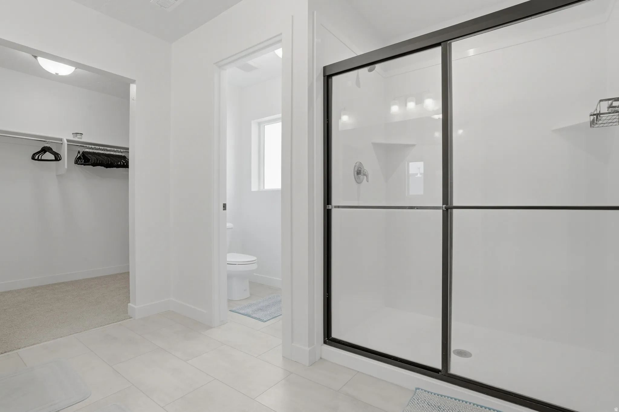 Modern bathroom featuring a glass-enclosed shower with black framing, light-toned tile flooring, and a separate water closet