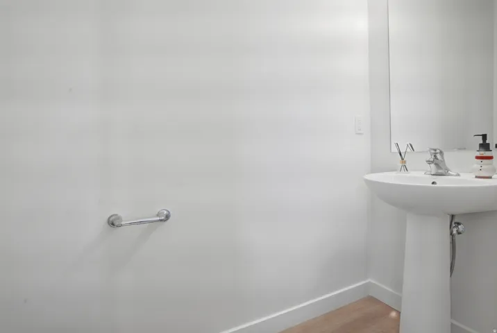 Pedestal sink with chrome faucet, mirror, wood-finish flooring, and white baseboards