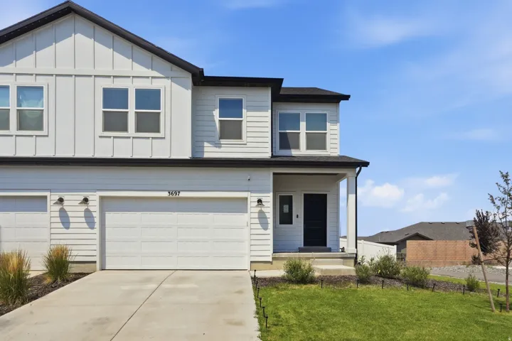 Modern exterior featuring white vertical and horizontal siding, a covered entry, a black front door, an attached garage, and a concrete driveway