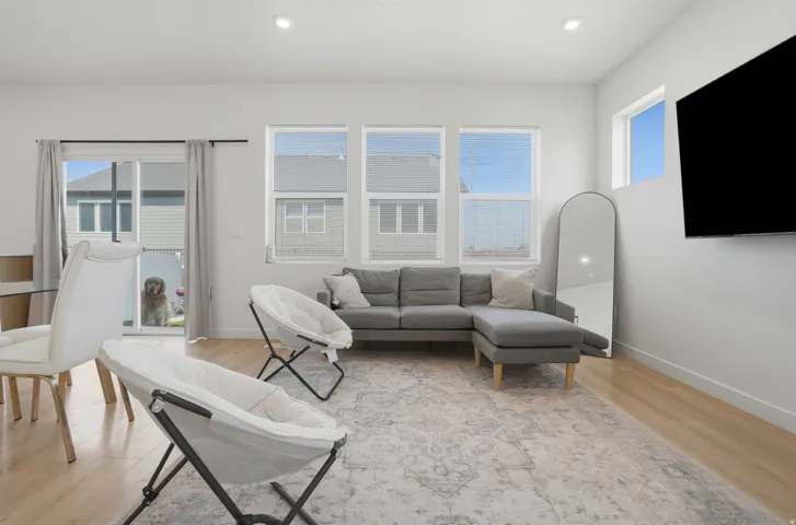 Living area featuring wood-finish flooring, recessed lighting, white walls, multiple windows with blinds, and a sliding glass door