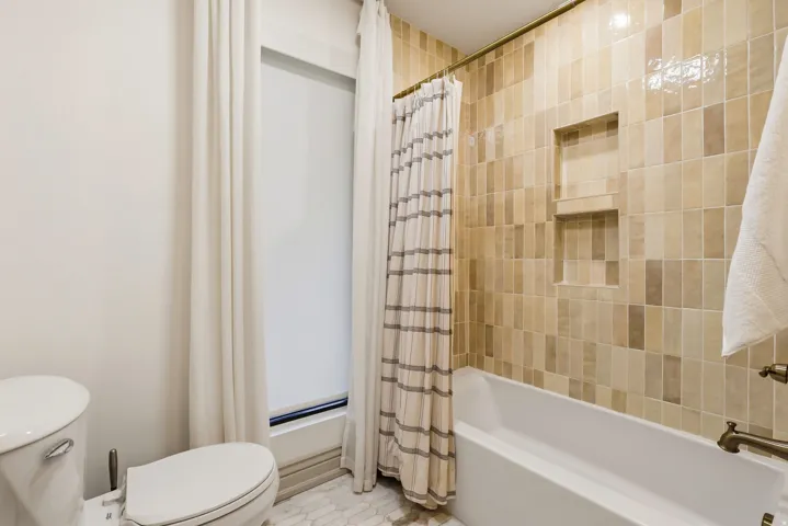 Bathroom featuring a full tub with shower, integrated wall niche shelving, and bronze-finish fixtures