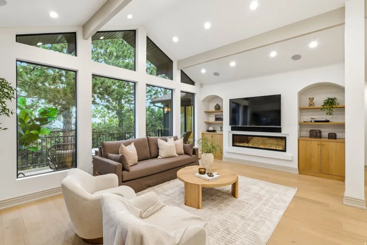 Spacious living area featuring a vaulted ceiling with exposed beams, recessed lighting, and large picture windows
