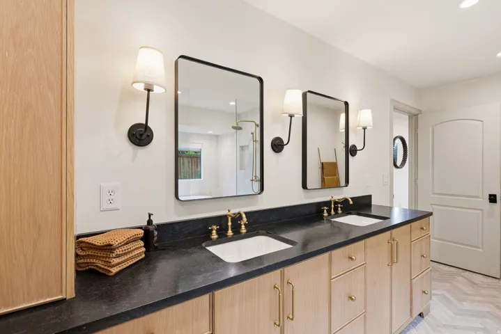 Double vanity with light wood-finish cabinetry, black countertops, and dual undermount sinks