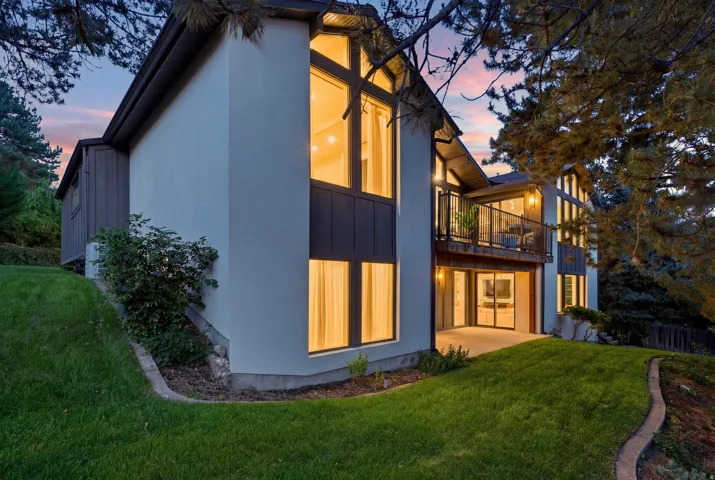 Multi-level residence featuring stucco and vertical siding, expansive windows, a glass-paneled balcony, and a ground-level patio
