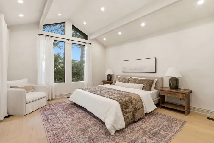 Vaulted ceiling with exposed beams, recessed lighting, expansive windows, wood-finish flooring, and white wall finishes