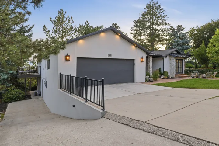 Contemporary exterior featuring a double garage, concrete driveway, stone facade accents, decorative outdoor lighting, and a terraced deck