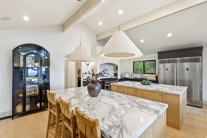 Gourmet kitchen featuring two large islands with white stone countertops, vaulted ceilings with exposed beams, recessed lighting, and stainless steel appliances including a large refrigerator