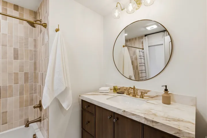 Bathroom featuring a dark wood-finish vanity with a single sink, a gold-toned faucet, and a patterned natural stone countertop