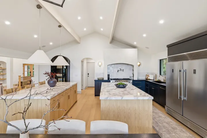 Gourmet kitchen featuring vaulted ceilings, recessed lighting, two marble-topped islands, premium stainless steel appliances, and wood-finish flooring