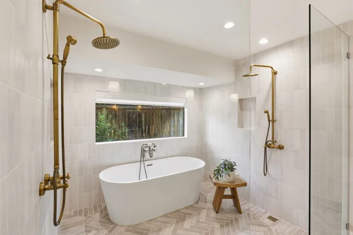 Bathroom featuring a freestanding soaking tub, a walk-in shower with a glass enclosure, dual shower systems with brass fixtures, and herringbone-patterned floor tiling