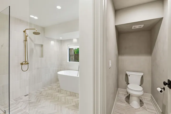 Bathroom featuring a freestanding tub, glass-enclosed shower with gold-finish fixtures, and herringbone-patterned tile flooring