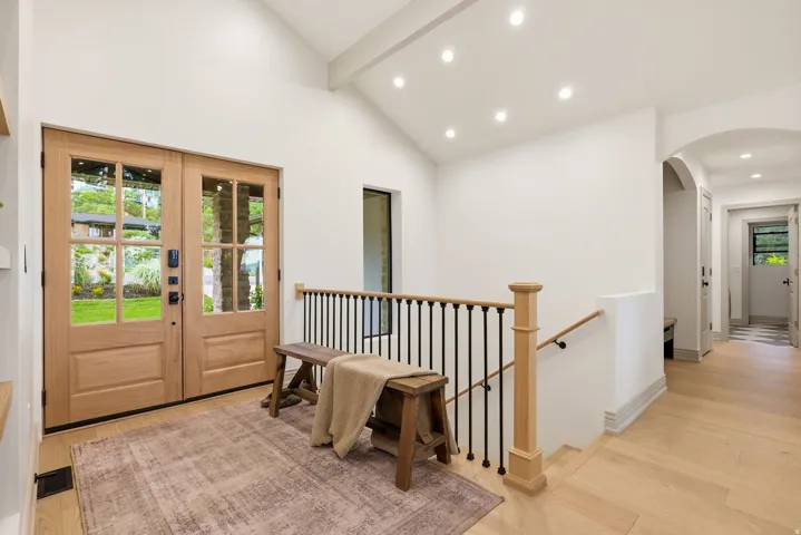 Double wood-paneled entry doors with glass lites, vaulted ceiling with recessed lighting, light wood-finish flooring, and black wrought iron stair railing