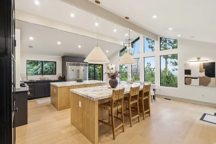 Expansive kitchen featuring dual islands with stone countertops, integrated stainless steel appliances, light wood-finish flooring, and a vaulted ceiling with recessed lighting