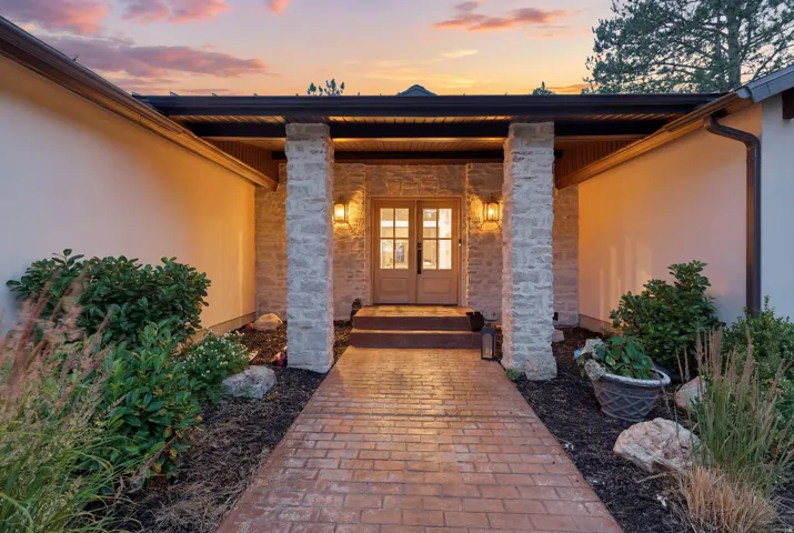 Entryway featuring a stamped concrete walkway, stone-clad columns, double wooden doors with glass inserts, and exterior wall sconces