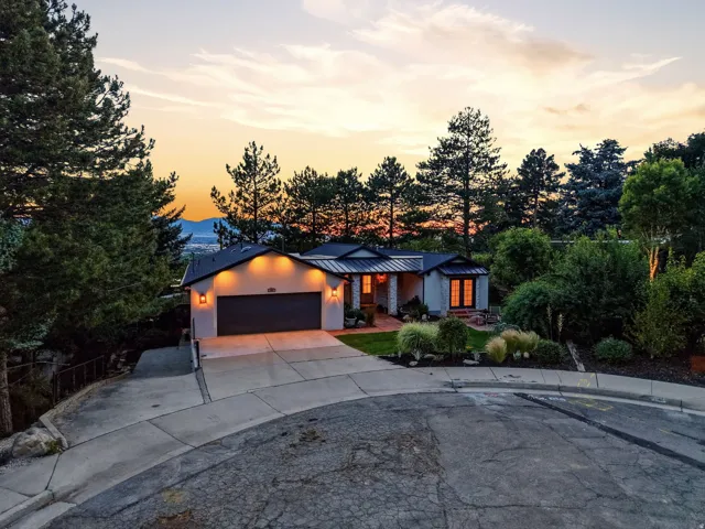 Stucco exterior residence featuring a two-car garage, black roof, and mature landscaping