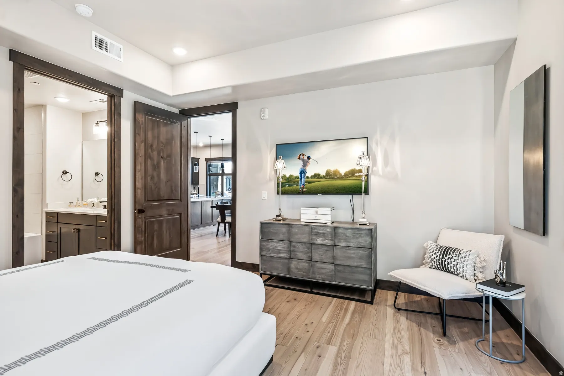 Wood-finish flooring throughout, with a recessed wall-mounted television and a contrasting dark wood door frame
