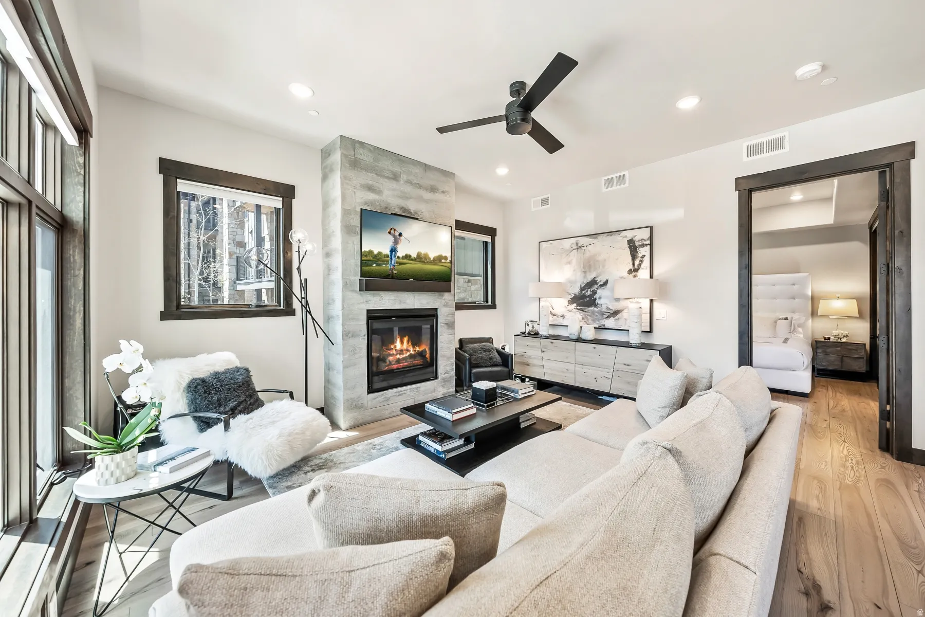 Spacious living area featuring light wood-finish flooring, a stone-clad fireplace with a built-in television, and recessed lighting