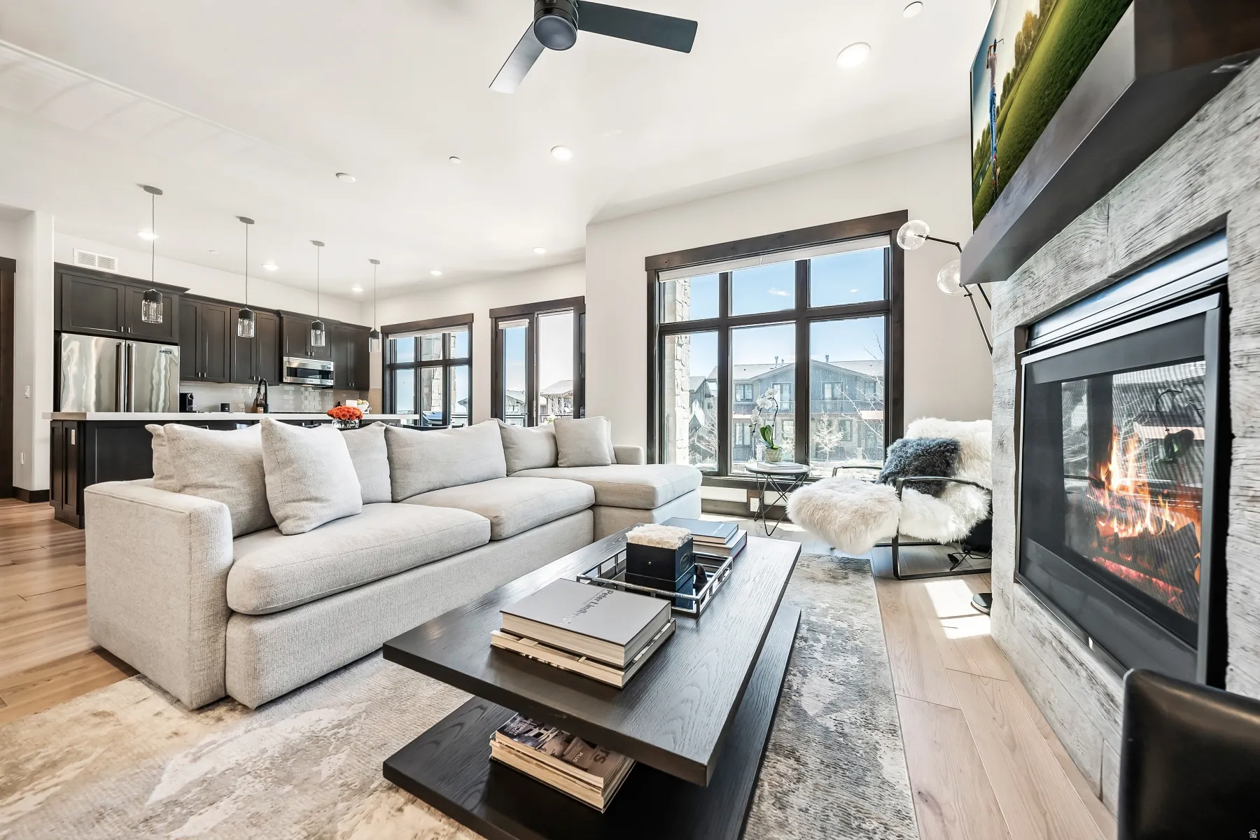 Open-concept living area with light wood-finish flooring, a contemporary fireplace with a stone-finish surround, and a ceiling fan