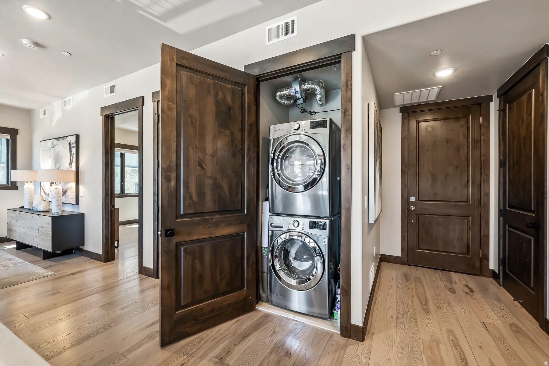 Dedicated laundry closet featuring a stacked washer and dryer, adjacent to an entryway with light wood-finish flooring