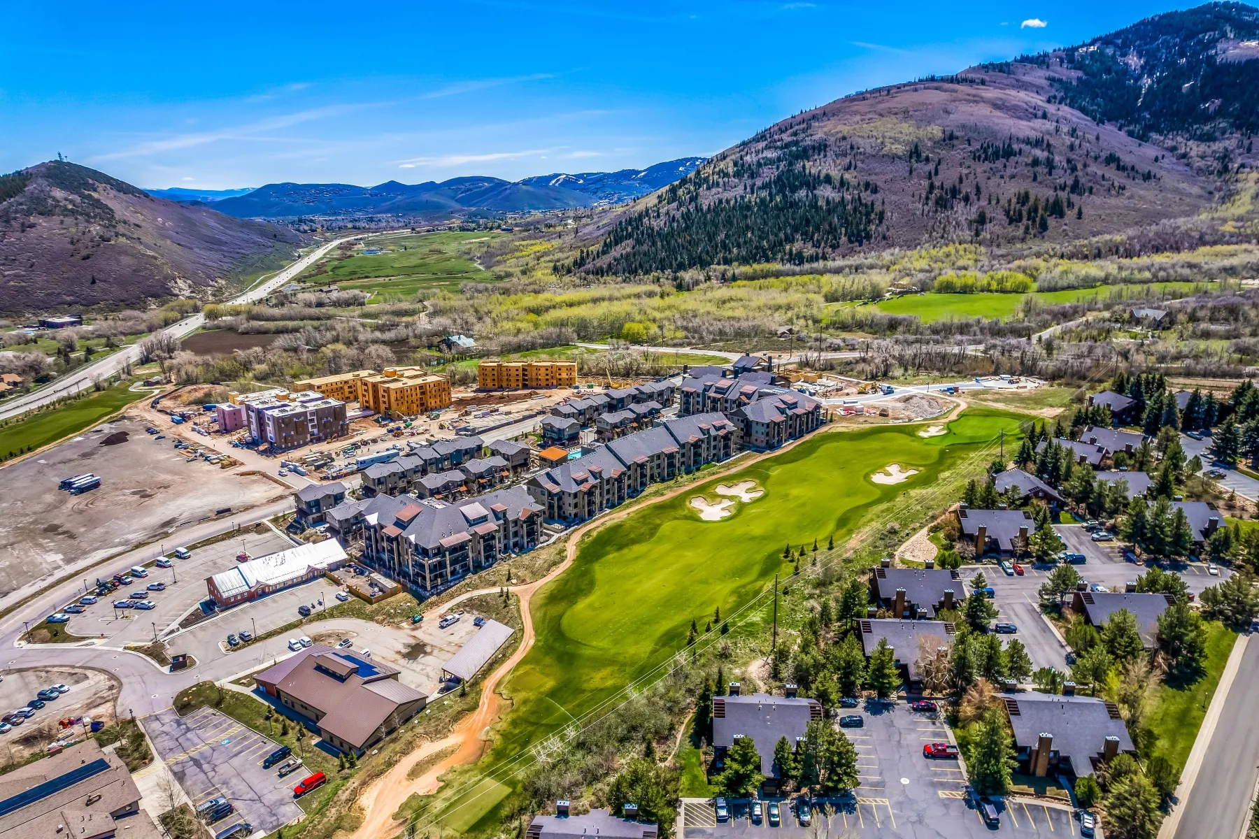 Aerial perspective showcasing a golf course, surrounding residential structures, and mountainous terrain