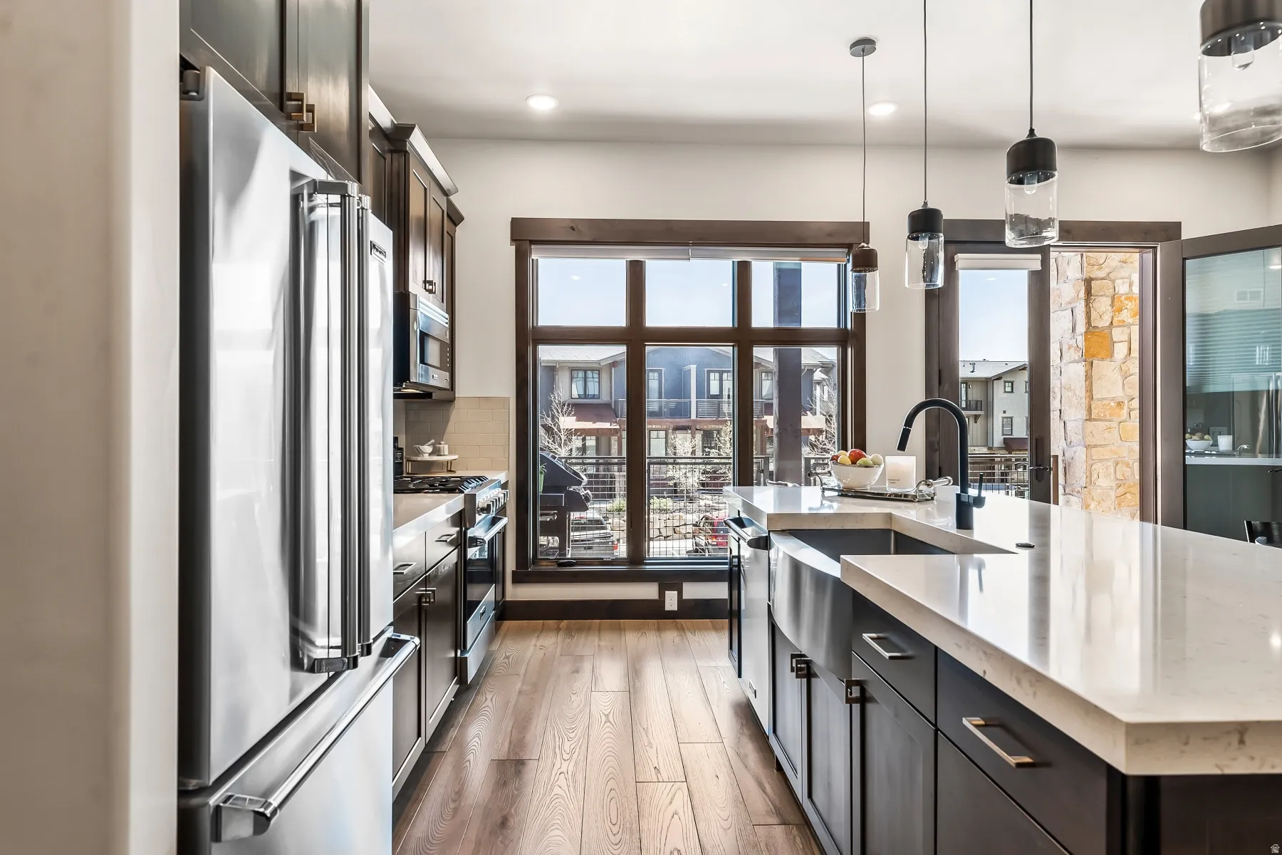 Gourmet kitchen featuring stainless steel appliances, dark wood-finish cabinetry, light stone countertops, and wood-finish flooring