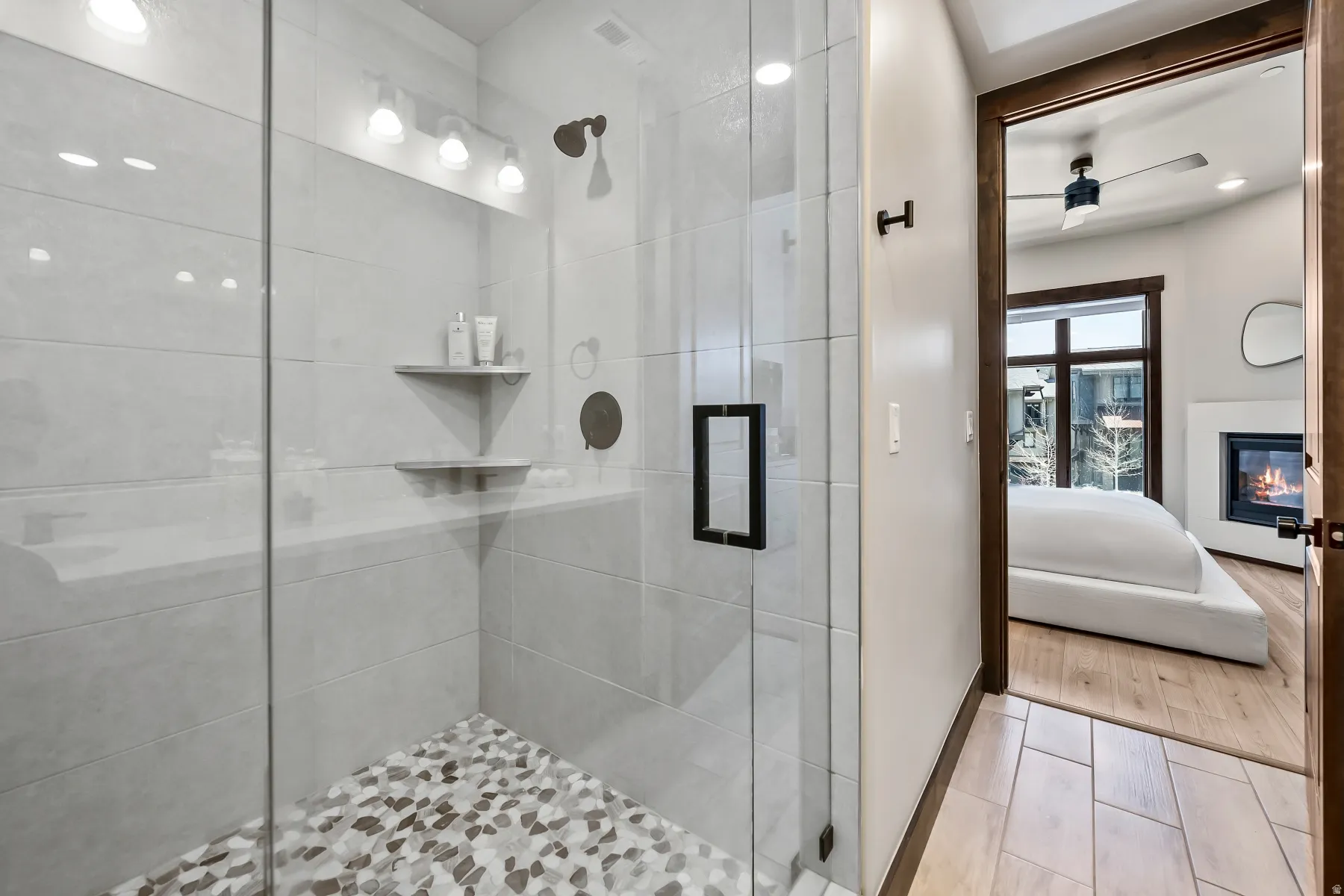 Glass-enclosed shower featuring large format tile walls and a pebble-style floor